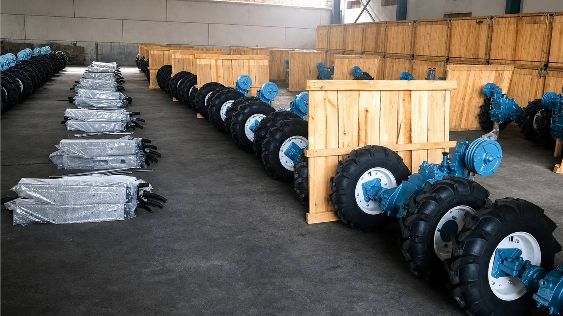 Rows of complete blue two-wheel tractors with wheel assemblies fitted, staged on a workshop floor beside wooden export crates