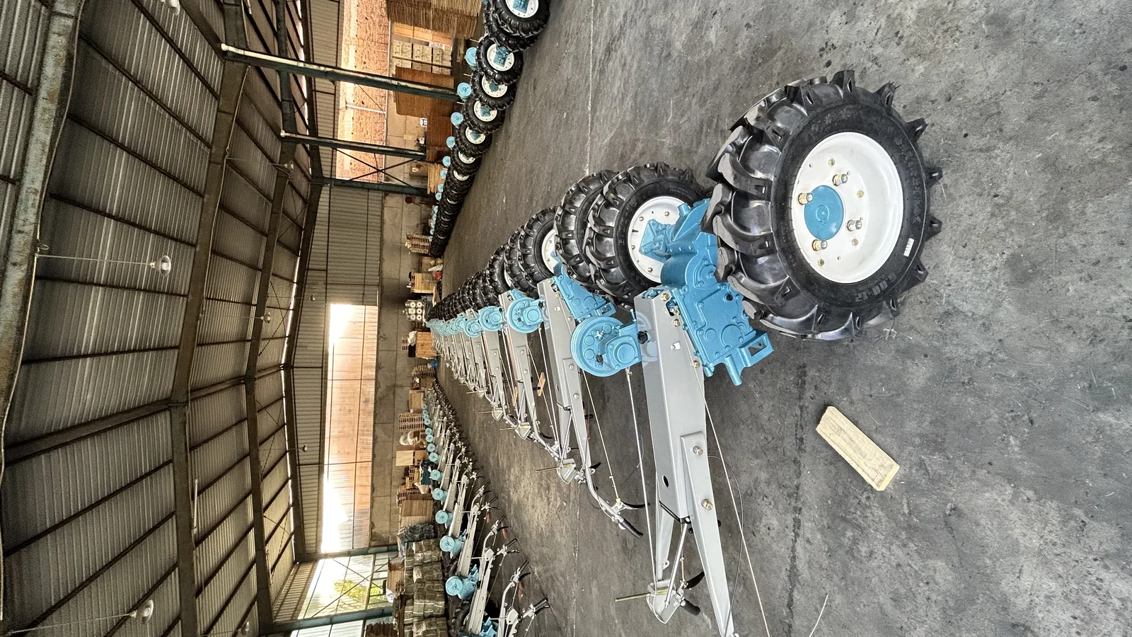 Rows of blue two-wheel tractors standing on a workshop floor with wooden export crates behind them, ready for shipment