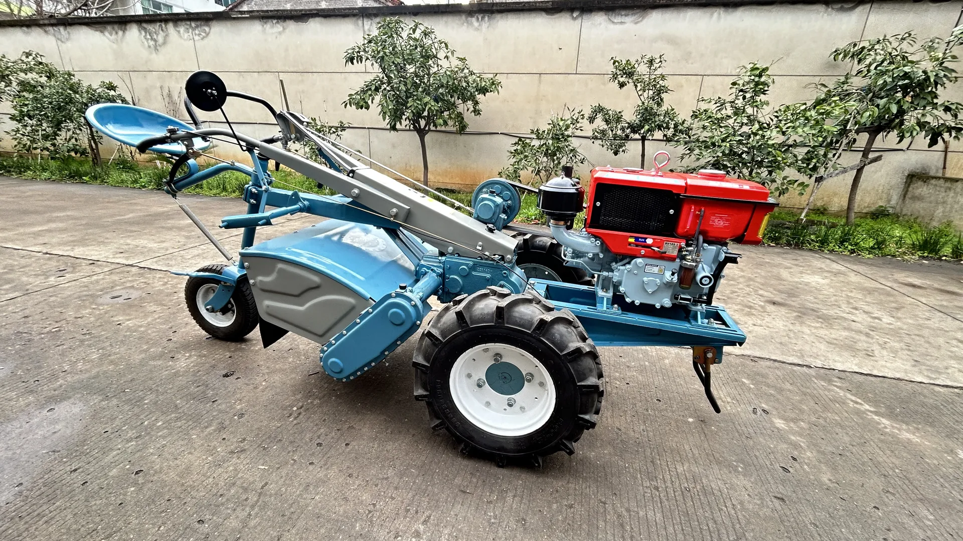 A blue GN12 two-wheel tractor chassis with its red single-cylinder diesel engine fitted, standing complete on a paved yard