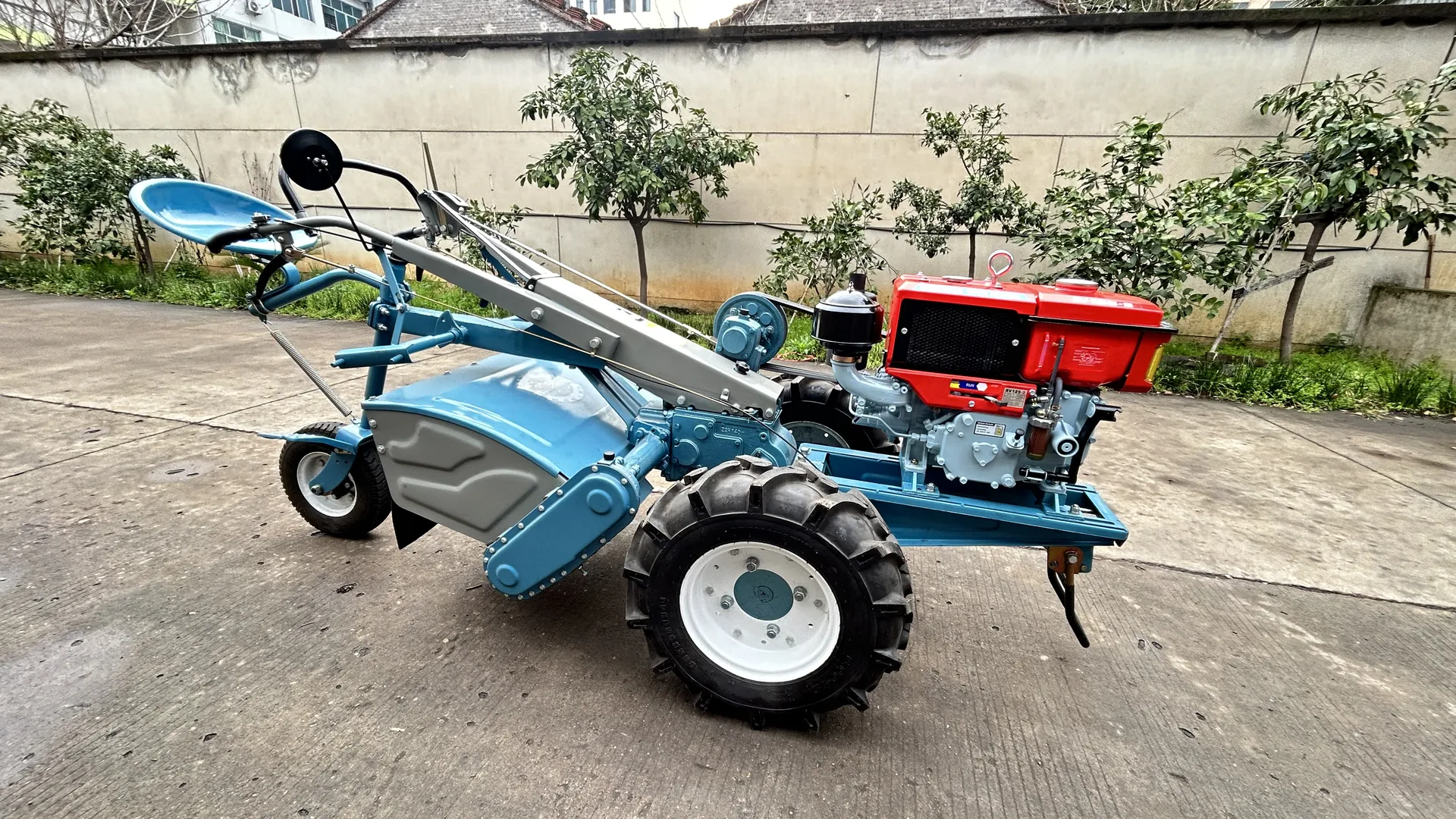 A blue SUNTEC two-wheel tractor with its rotary tiller implement mounted, photographed in the yard before delivery